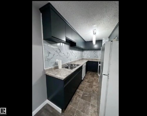 Kitchen featuring white appliances, dark cabinets, and a textured ceiling - 302 49 Akins Drive, St. Albert, AB - Indoor Photo Showing Kitchen With Double Sink