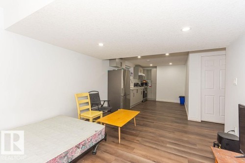 Bedroom featuring dark wood-style floors, freestanding refrigerator, recessed lighting, and a textured ceiling - 3128 13 Avenue, Edmonton, AB - Indoor