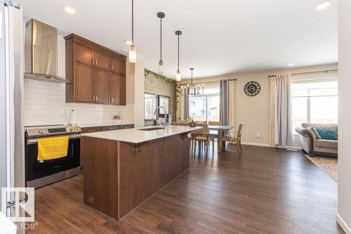 Kitchen with stainless steel appliances, decorative light fixtures, backsplash, dark wood-style flooring, and a breakfast bar - 3128 13 Avenue, Edmonton, AB - Indoor Photo Showing Kitchen With Upgraded Kitchen