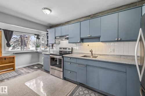Kitchen featuring stainless steel appliances, backsplash, light countertops, blue cabinetry, and light wood-type flooring - 5911 119 Avenue, Edmonton, AB - Indoor Photo Showing Kitchen