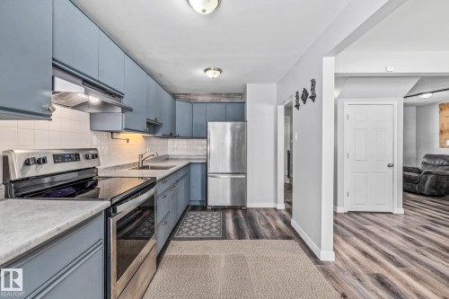 Kitchen featuring stainless steel appliances, light countertops, backsplash, dark wood-style flooring, and blue cabinets - 5911 119 Avenue, Edmonton, AB - Indoor Photo Showing Kitchen