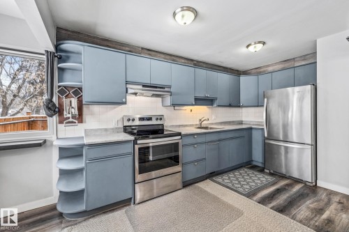 Kitchen featuring open shelves, stainless steel appliances, decorative backsplash, dark wood-style floors, and blue cabinets - 5911 119 Avenue, Edmonton, AB - Indoor Photo Showing Kitchen