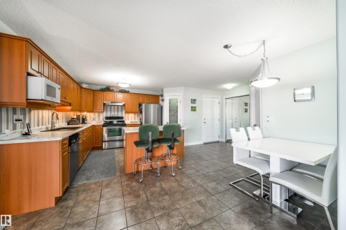 Kitchen with stainless steel appliances, light countertops, a kitchen island, wood finish cabinets, and a breakfast bar area - 402 7803 Golf Course Road, Stony Plain, AB - Indoor Photo Showing Kitchen