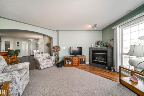 Living room with arched walkways, a tile fireplace, crown molding, and wood finished floors - 402 7803 Golf Course Road, Stony Plain, AB - Indoor Photo Showing Living Room With Fireplace
