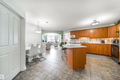 Kitchen with arched walkways, light countertops, wood finish cabinets, a center island, and a breakfast bar - 402 7803 Golf Course Road, Stony Plain, AB - Indoor Photo Showing Kitchen