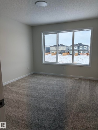 Carpeted empty room featuring a textured ceiling and a residential view - 5756 Hawthorn Common, Edmonton, AB - Indoor Photo Showing Other Room