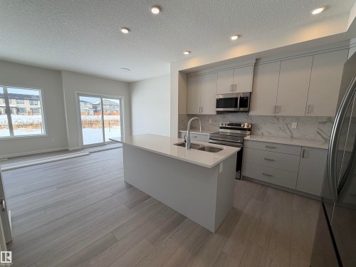Kitchen with modern cabinets, stainless steel appliances, gray cabinetry, light wood-style floors, and light stone counters - 5756 Hawthorn Common, Edmonton, AB - Indoor Photo Showing Kitchen With Double Sink