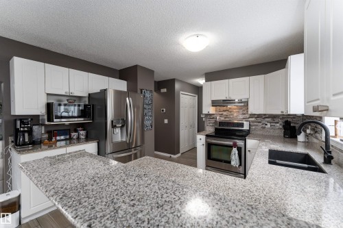 Kitchen featuring stainless steel appliances, white cabinetry, light stone countertops, a textured ceiling, and a peninsula - 31 Haviland Crescent, St. Albert, AB - Indoor Photo Showing Kitchen With Double Sink