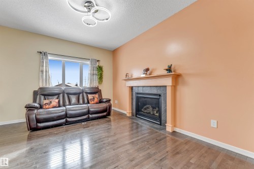 Living room with wood-type flooring, a tiled fireplace, and a textured ceiling - 3449 28 Street, Edmonton, AB - Indoor Photo Showing Living Room With Fireplace