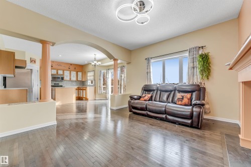Living area featuring arched walkways, hanging lights, decorative columns, light wood-type flooring, and a textured ceiling - 3449 28 Street, Edmonton, AB - Indoor Photo Showing Other Room