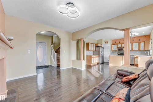 Living room with decorative columns, light wood-style flooring, arched walkways, and a textured ceiling - 3449 28 Street, Edmonton, AB - Indoor Photo Showing Living Room
