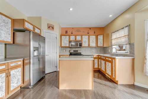 Kitchen with stainless steel appliances, a kitchen island, light countertops, light wood finished floors, and a textured ceiling - 3449 28 Street, Edmonton, AB - Indoor Photo Showing Kitchen