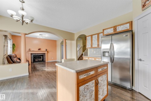 Kitchen featuring stainless steel refrigerator with ice dispenser, a kitchen island, light countertops, open floor plan, and wood finish cabinetry - 3449 28 Street, Edmonton, AB - Indoor With Fireplace