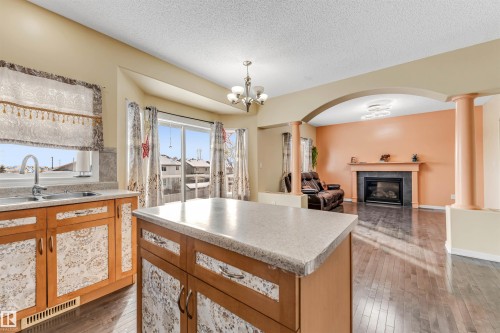 Kitchen with arched walkways, light countertops, light wood finished floors, a glass covered fireplace, and a textured ceiling - 3449 28 Street, Edmonton, AB - Indoor With Fireplace