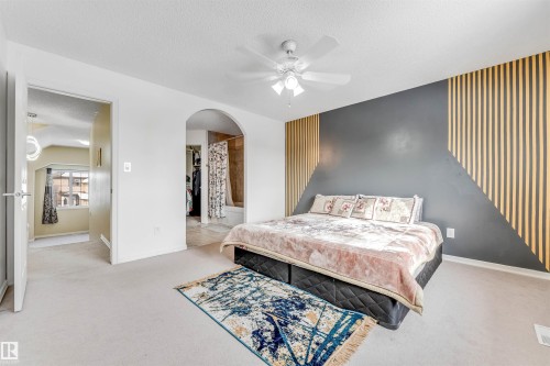 Bedroom with a textured ceiling, light carpet, an accent wall, ceiling fan, and arched walkways - 3449 28 Street, Edmonton, AB - Indoor Photo Showing Bedroom