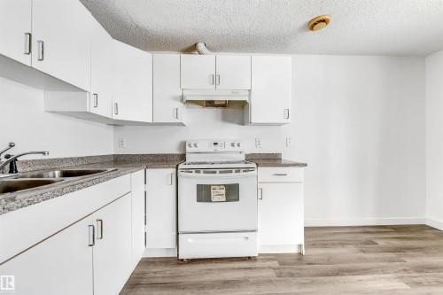 Kitchen with white electric range oven, white cabinets, light wood finished floors, a textured ceiling, and dark countertops - 3449 28 Street, Edmonton, AB - Indoor Photo Showing Kitchen With Double Sink