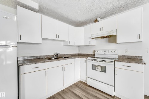 Kitchen with white appliances, a textured ceiling, white cabinetry, dark countertops, and light wood-style floors - 3449 28 Street, Edmonton, AB - Indoor Photo Showing Kitchen With Double Sink