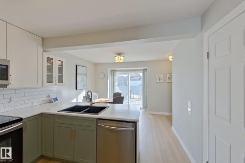 Kitchen with a peninsula, stainless steel appliances, glass insert cabinets, decorative backsplash, and light wood-style flooring - 121 1 Aberdeen Way, Stony Plain, AB - Indoor Photo Showing Kitchen With Double Sink