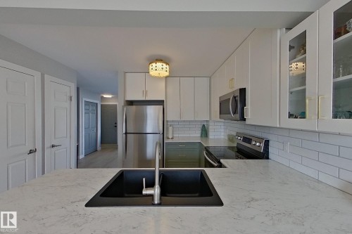 Kitchen with glass insert cabinets, stainless steel appliances, white cabinetry, light stone countertops, and tasteful backsplash - 121 1 Aberdeen Way, Stony Plain, AB - Indoor Photo Showing Kitchen With Stainless Steel Kitchen With Double Sink