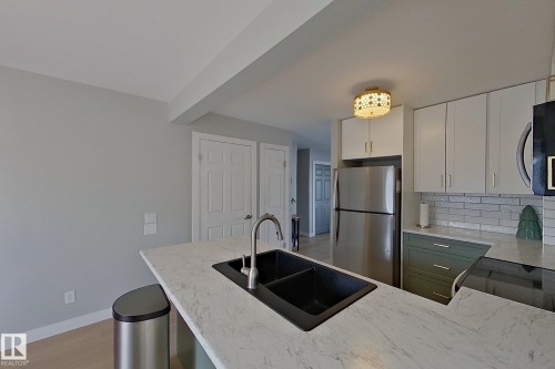 Kitchen featuring stainless steel appliances, white cabinets, backsplash, a peninsula, and light stone counters - 121 1 Aberdeen Way, Stony Plain, AB - Indoor Photo Showing Kitchen With Stainless Steel Kitchen With Double Sink