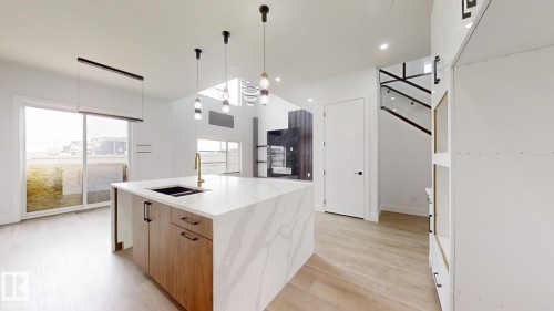 Kitchen with hanging light fixtures, light stone countertops, modern cabinets, light wood finished floors, and an island with sink - 1707 18 Street, Edmonton, AB - Indoor Photo Showing Kitchen With Double Sink