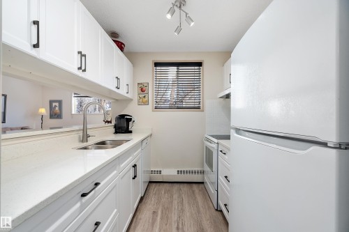 Kitchen featuring white appliances, white cabinetry, light stone counters, and light floors - 116 11620 9A Avenue, Edmonton, AB - Indoor Photo Showing Kitchen With Double Sink