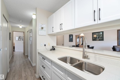 Kitchen featuring white cabinetry, a textured ceiling, light stone counters, and light flooring - 116 11620 9A Avenue, Edmonton, AB - Indoor Photo Showing Kitchen With Double Sink