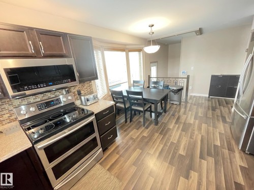 Kitchen with stainless steel appliances, decorative light fixtures, tasteful backsplash, dark wood-type flooring, and light stone counters - 324 Warwick Road, Edmonton, AB - Indoor Photo Showing Other Room