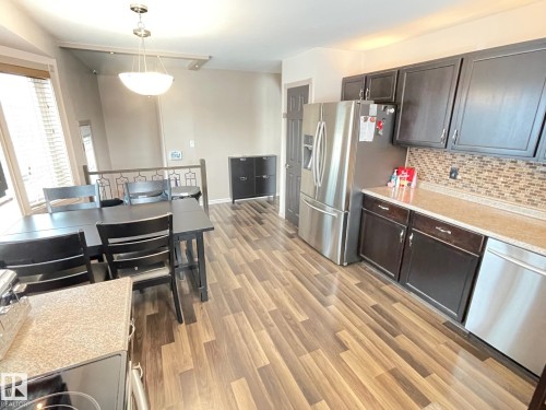 Kitchen featuring stainless steel appliances, dark wood finish cabinetry, light wood-style flooring, hanging light fixtures, and tasteful backsplash - 324 Warwick Road, Edmonton, AB - Indoor Photo Showing Kitchen