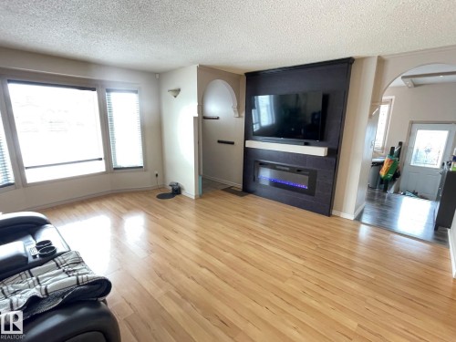 Living area featuring arched walkways, light wood-style floors, a textured ceiling, and a large fireplace - 324 Warwick Road, Edmonton, AB - Indoor Photo Showing Living Room