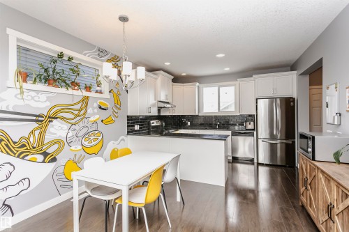Dual tone kitchen with stainless steel appliances, dark wood-type flooring, tasteful backsplash, two tone cabinets, and dark stone counters - 16420 15 Avenue, Edmonton, AB - Indoor