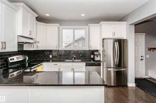 Kitchen with stainless steel appliances, dark stone countertops, white cabinets, a peninsula, and dark wood-style floors - 16420 15 Avenue, Edmonton, AB - Indoor Photo Showing Kitchen With Upgraded Kitchen