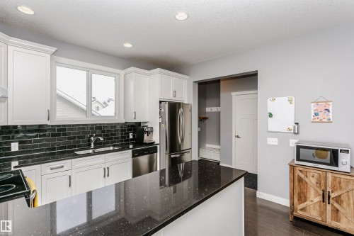 Kitchen featuring stainless steel appliances, white cabinets, dark stone counters, dark wood finished floors, and decorative backsplash - 16420 15 Avenue, Edmonton, AB - Indoor Photo Showing Kitchen With Upgraded Kitchen