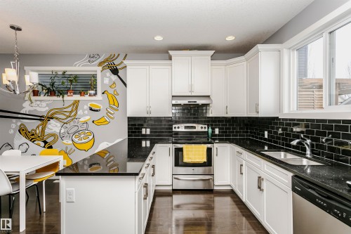 Kitchen featuring a peninsula, dark stone countertops, stainless steel appliances, white cabinetry, and decorative light fixtures - 16420 15 Avenue, Edmonton, AB - Indoor Photo Showing Kitchen With Upgraded Kitchen