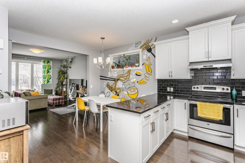 Kitchen featuring stainless steel electric range oven, a peninsula, open floor plan, dark stone countertops, and white cabinets - 16420 15 Avenue, Edmonton, AB - Indoor Photo Showing Kitchen With Upgraded Kitchen