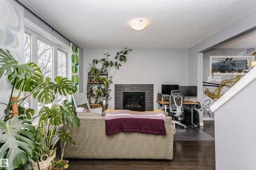 Living area with a desk, a glass covered fireplace, dark wood-style flooring, and a textured ceiling - 16420 15 Avenue, Edmonton, AB - Indoor With Fireplace