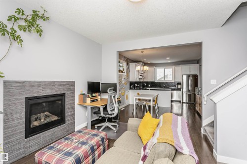 Living room featuring a fireplace, an office area, dark wood finished floors, a textured ceiling, and suspended lighting - 16420 15 Avenue, Edmonton, AB - Indoor Photo Showing Living Room With Fireplace