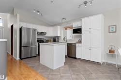 Kitchen featuring stainless steel appliances, light countertops, white cabinets, vaulted ceiling, and a center island - 
