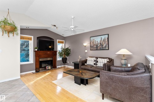 Living room featuring a ceiling fan, lofted ceiling, a fireplace with raised hearth, and light wood-style flooring - 357 Blackburn Drive E, Edmonton, AB - Indoor Photo Showing Living Room With Fireplace