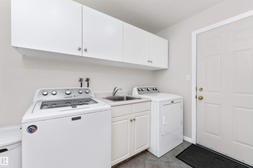 Laundry room featuring cabinet space, washing machine and dryer, a textured ceiling, and light tile patterned flooring - 357 Blackburn Drive E, Edmonton, AB - Indoor Photo Showing Laundry Room