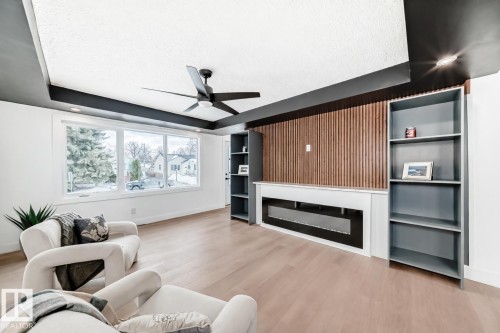 Living area with ceiling fan, a glass covered fireplace, light wood-style flooring, built in features, and a raised ceiling - 8712 89 Avenue, Edmonton, AB - Indoor Photo Showing Living Room With Fireplace