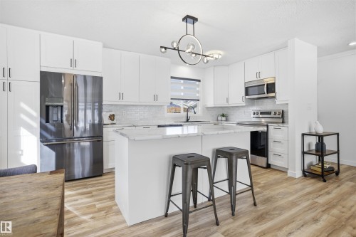 Kitchen featuring stainless steel appliances, a kitchen bar, a center island, white cabinets, and light stone countertops - 4204 41B Street, Leduc, AB - Indoor Photo Showing Kitchen With Upgraded Kitchen