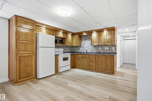 Kitchen with wood finish cabinets, white appliances, a drop ceiling, light wood-style floors, and decorative backsplash - 4204 41B Street, Leduc, AB - Indoor Photo Showing Kitchen