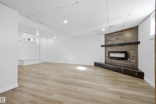 Unfurnished living room with a paneled ceiling, light wood-type flooring, and a tiled fireplace - 4204 41B Street, Leduc, AB - Indoor Photo Showing Other Room With Fireplace