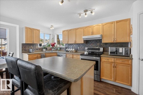 Kitchen featuring stainless steel appliances, light wood finish cabinets, dark wood-style flooring, a center island, and a kitchen bar - 4519 Turner Square Square, Edmonton, AB - Indoor Photo Showing Kitchen With Double Sink