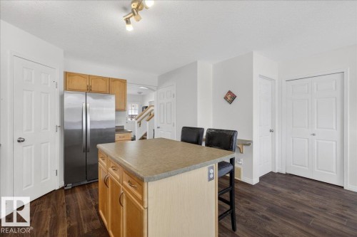 Kitchen with freestanding refrigerator, a kitchen breakfast bar, a kitchen island, a textured ceiling, and dark wood finished floors - 4519 Turner Square Square, Edmonton, AB - Indoor Photo Showing Kitchen