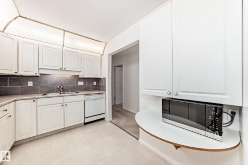 Kitchen with white cabinets, stainless steel microwave, light floors, white dishwasher, and backsplash - 118 6220 Fulton Road, Edmonton, AB - Indoor Photo Showing Kitchen With Double Sink