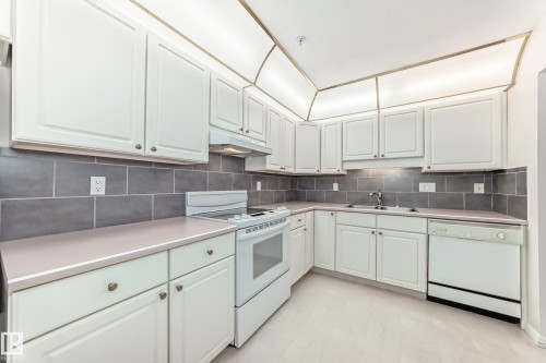 Kitchen featuring white appliances, light flooring, light countertops, tasteful backsplash, and white cabinets - 118 6220 Fulton Road, Edmonton, AB - Indoor Photo Showing Kitchen With Double Sink