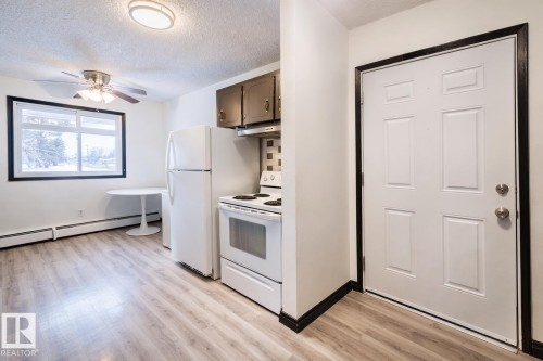 Kitchen featuring white appliances, a textured ceiling, a ceiling fan, light wood finished floors, and baseboard heating - 3917/3919 54 Street, Wetaskiwin, AB - Indoor Photo Showing Kitchen