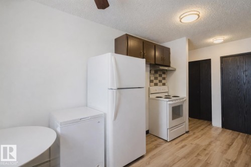 Kitchen featuring white appliances, decorative backsplash, a textured ceiling, light wood-style flooring, and dark wood finish cabinetry - 3917/3919 54 Street, Wetaskiwin, AB - Indoor Photo Showing Kitchen